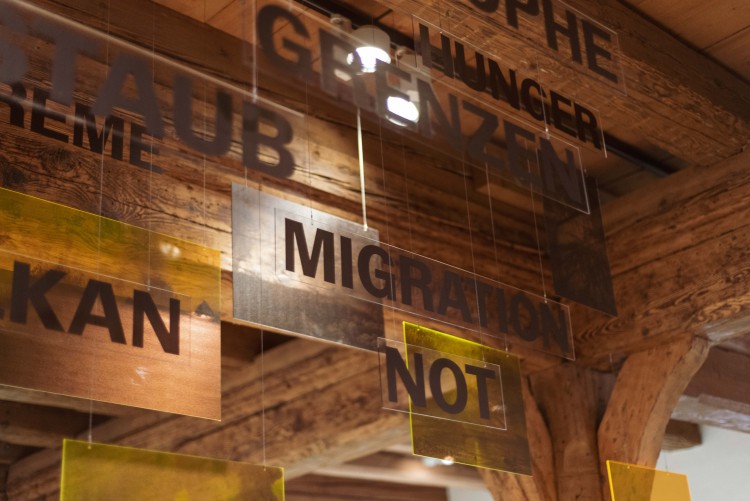 Tafeln aus Plastik hängen an einer Decke darauf die Wörter; Grenzen, Migration, Not und Hunger