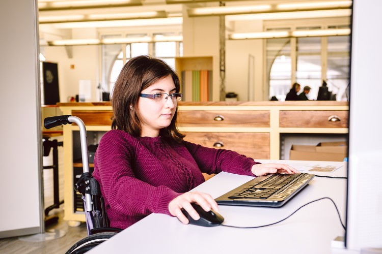 Junge Frau in einem Rollstuhl bedient einen Computer