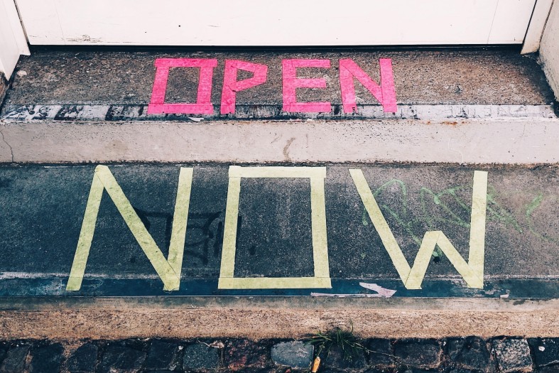 Schriftzug "Open Now" mit Klebeband vor einer Eingangstür