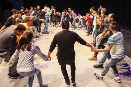 Veschiedene Menschen tanzen zusammen im Kreis, halten sich an den Händen