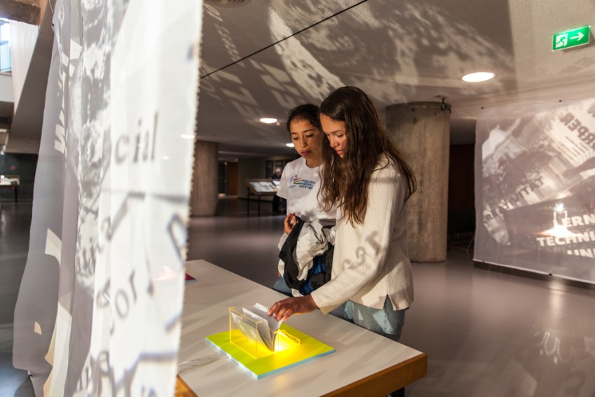 Zwei Jugendliche stehen vor einem Tisch in einer Ausstellung und blättern durch Karteikarten